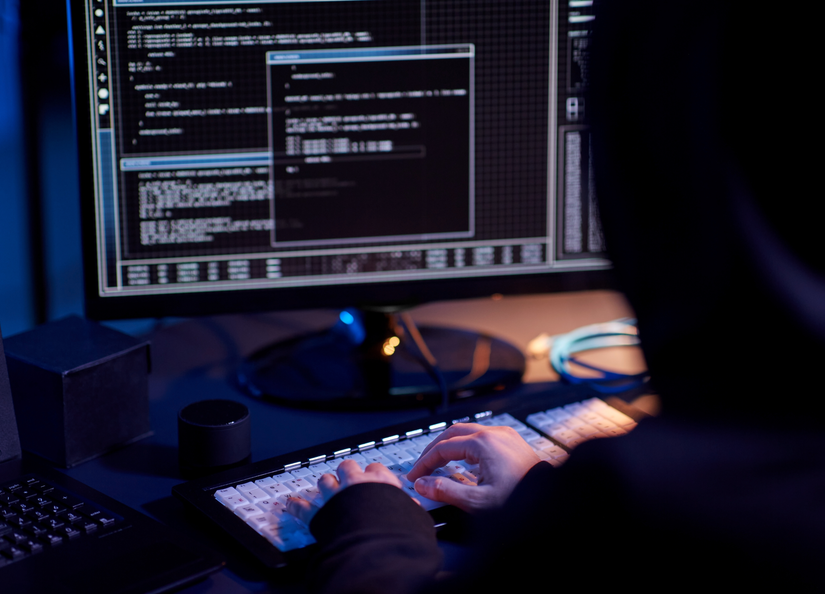 A hooded person sitting at a computer investigating data.