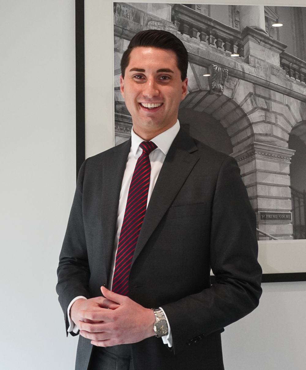 A young caucasian male lawyer dressed in a suit posing for a photo infront of a black and white print