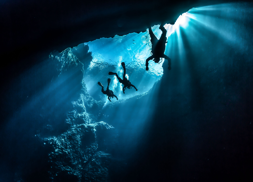 Three people diving deep underwater in a cave