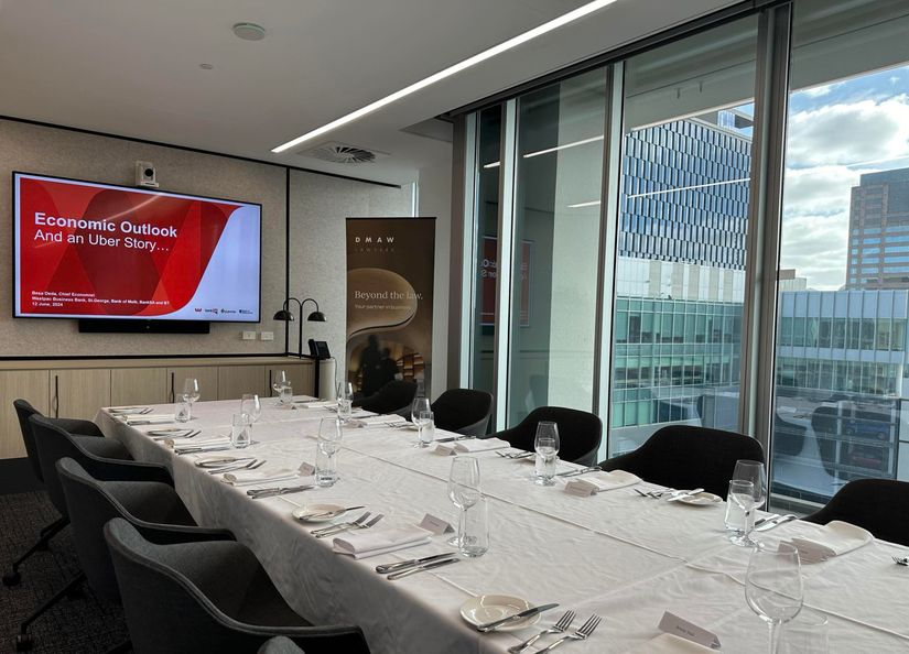 A boardroom table set for lunch with a presentation ready to go on the screen and a company banner set up in the corner