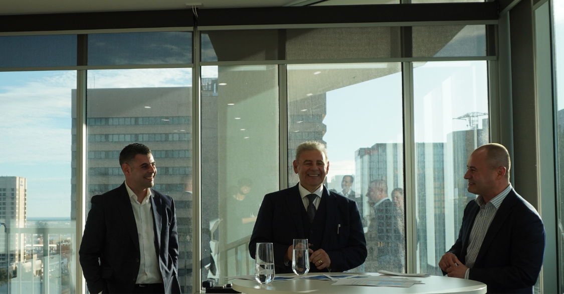 Three professional men looking happy, giving a presentation to a group with the Adelaide city scape in the background