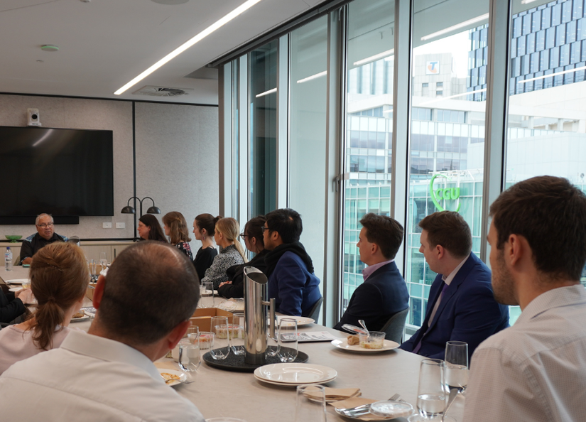 Group of professionals seated at boardroom table with their lunch listening to a presentation