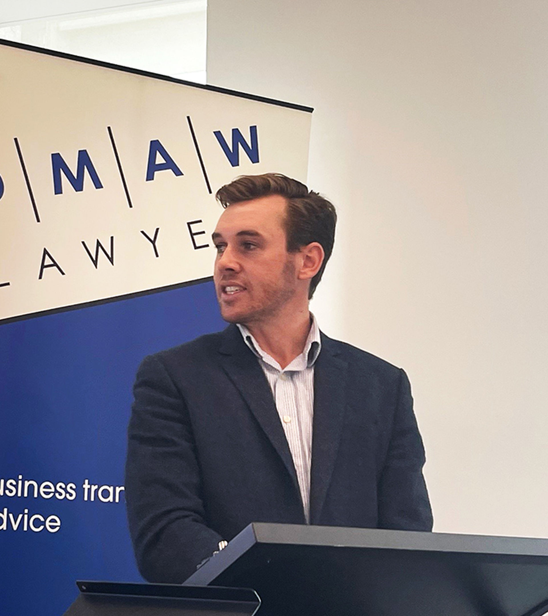 Man giving presentation with DMAW Lawyers' banner in background