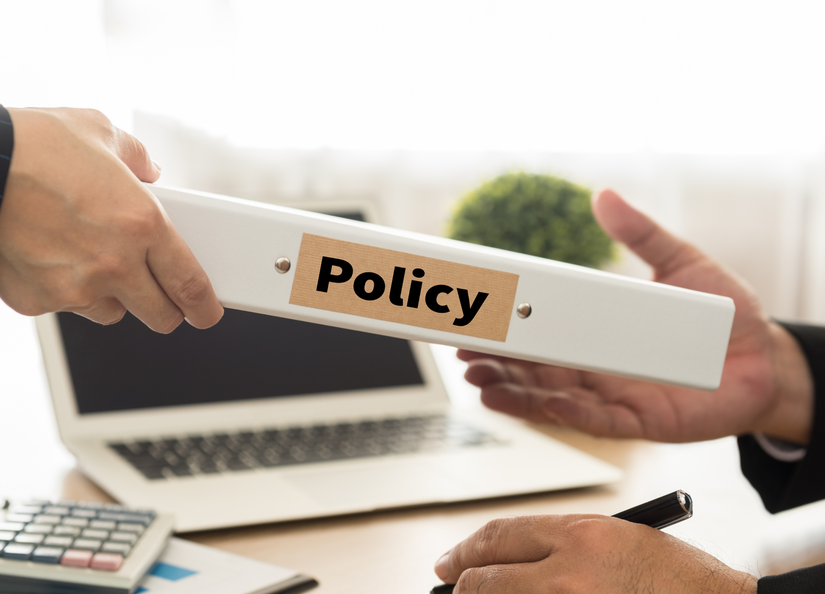 Someone passing their colleague a folder with "Policy" written on the side