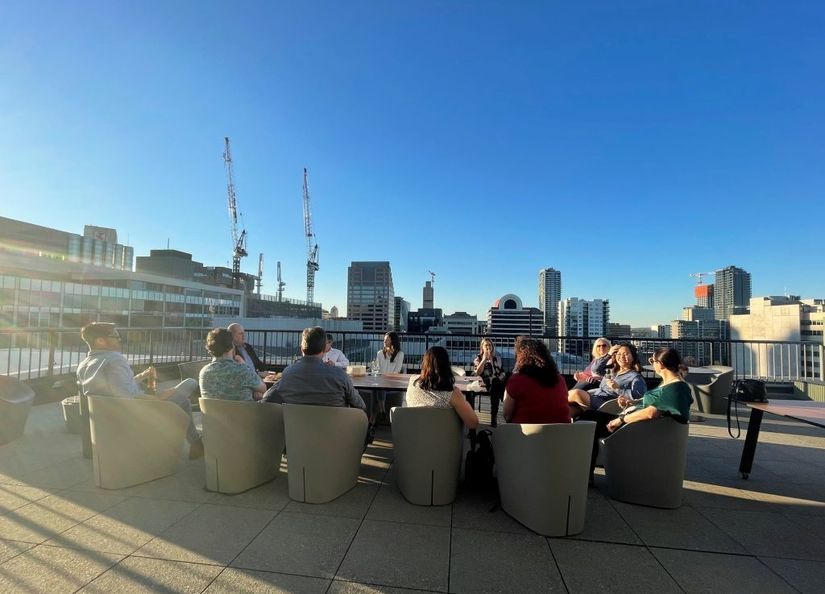 Group of staff enjoying a beverage, sitting around a table on the rooftop overlooking Adelaide CBD
