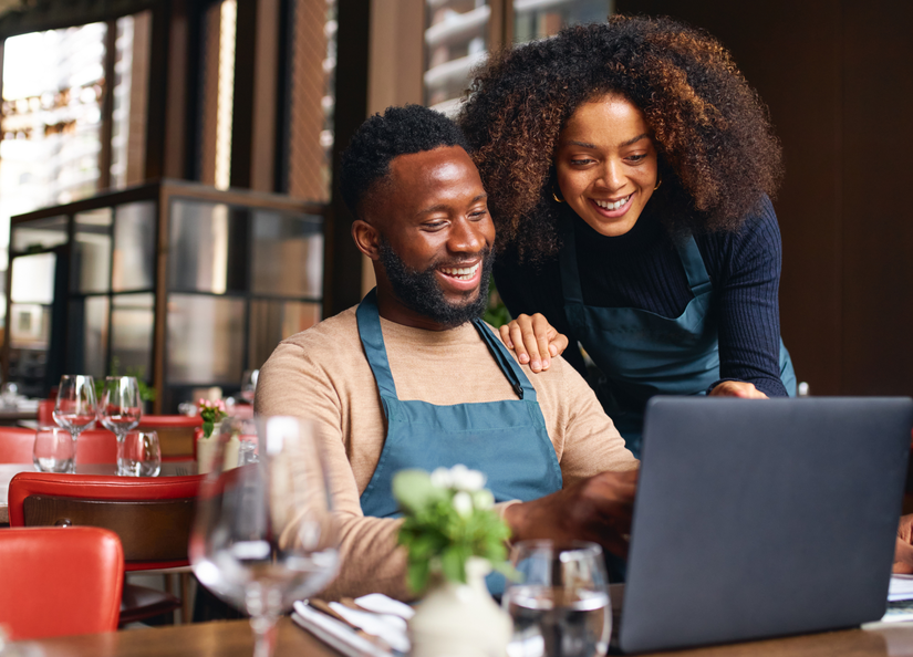 Man and woman of African-american descent looking at a laptop screen together in a restaurant setting