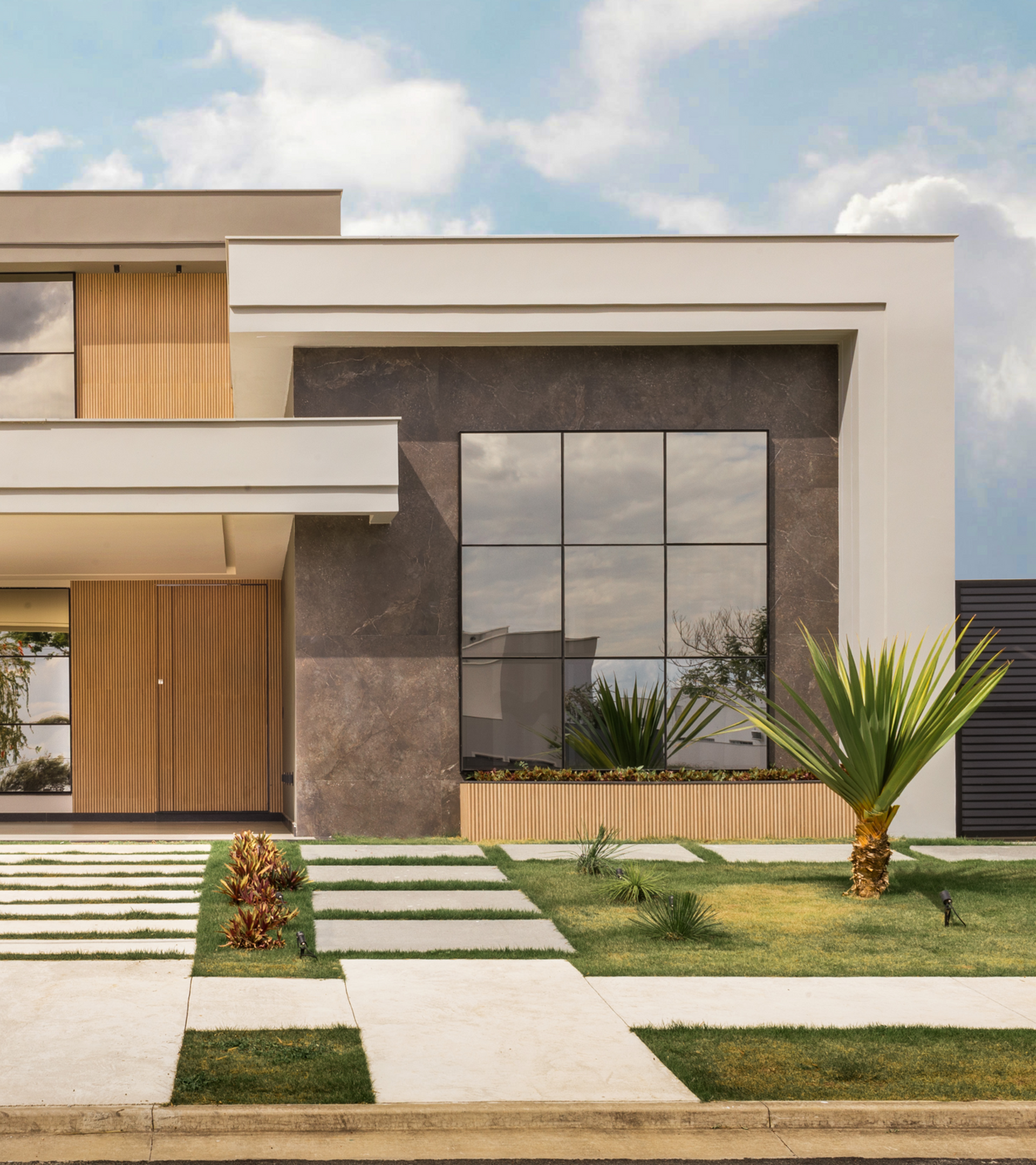 A modern two story bungalow with cream, grey and wooden furnishings. It has a small front yard with grass, shrubs and a path to the door.