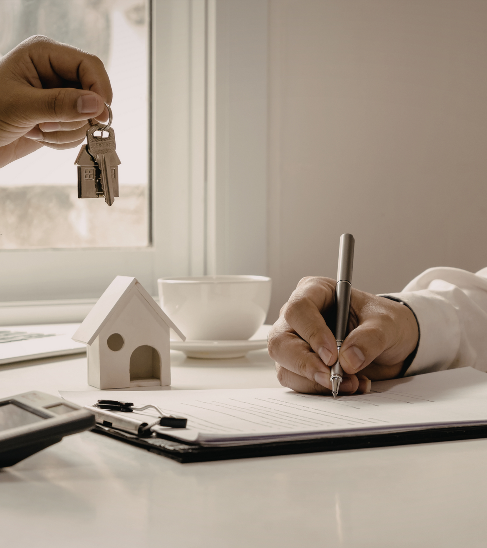 A hand passing over some keys and another hand signing a contract