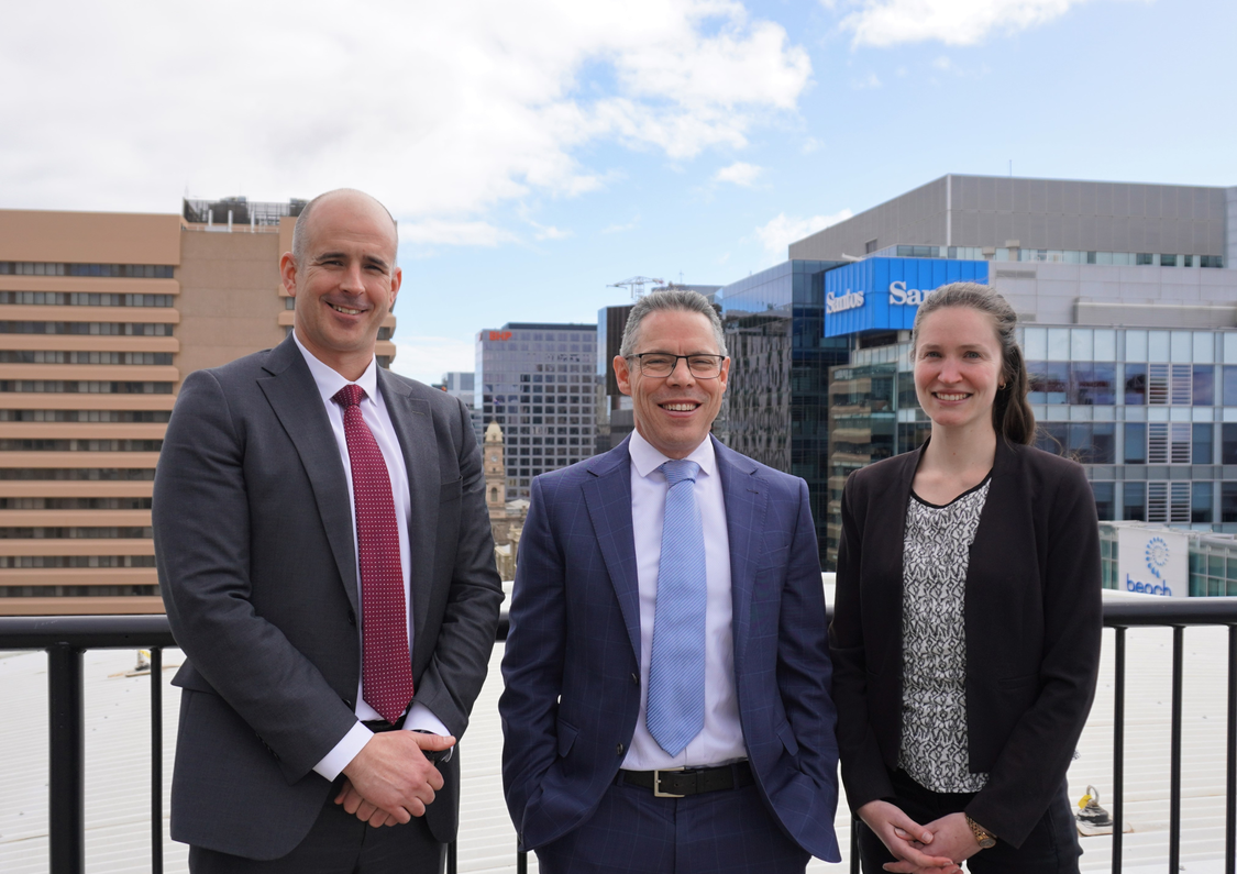 Image of two men and a woman in business attire on a rooftop with the cityscape in the background