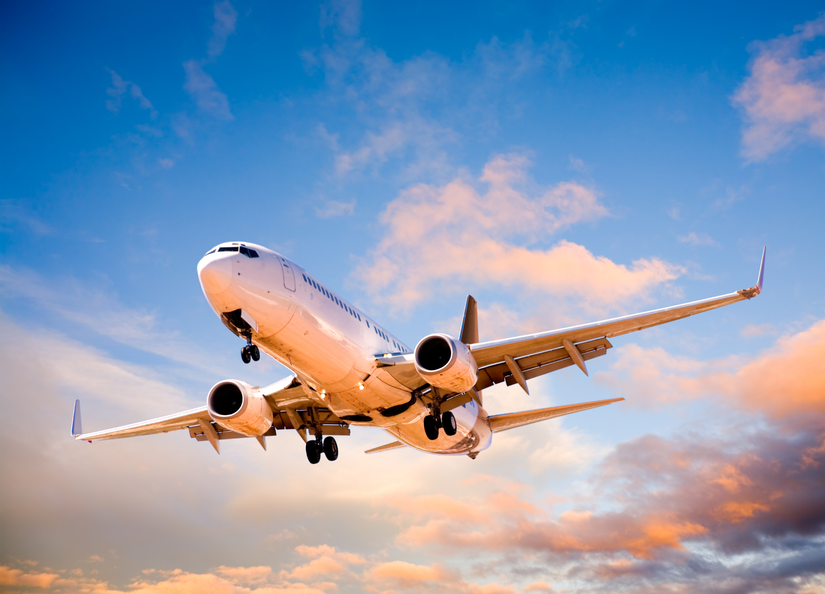 Stock image of white airplane in a blue sky with clouds and sun