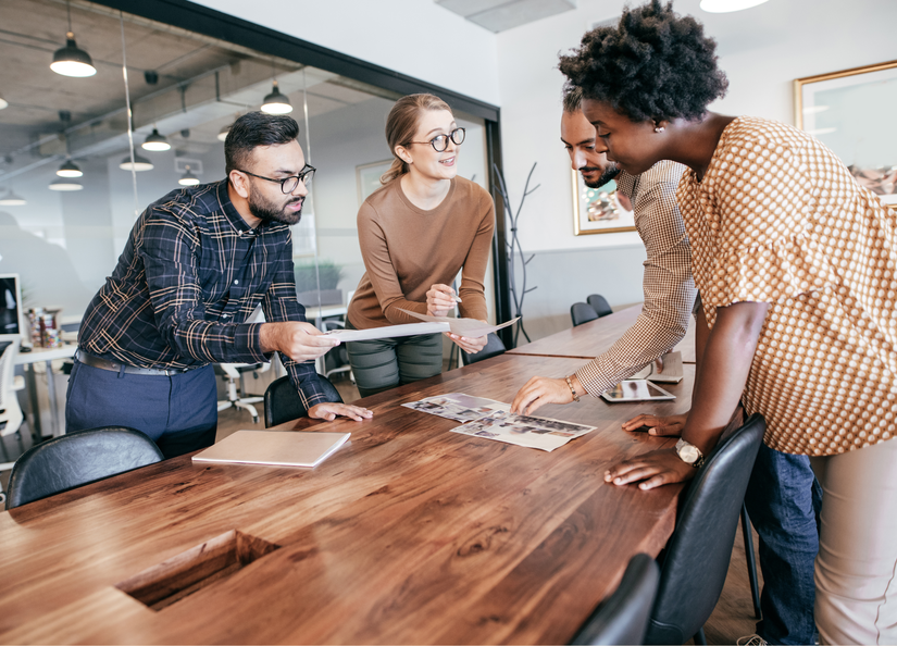 A group of staff leaning over a boardroom table discussing something