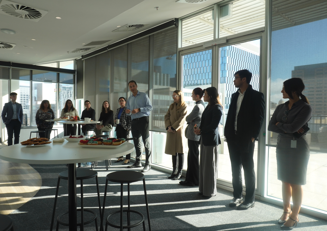 A group of professionals gathered at a morning tea, respectfully listening to a speaker.