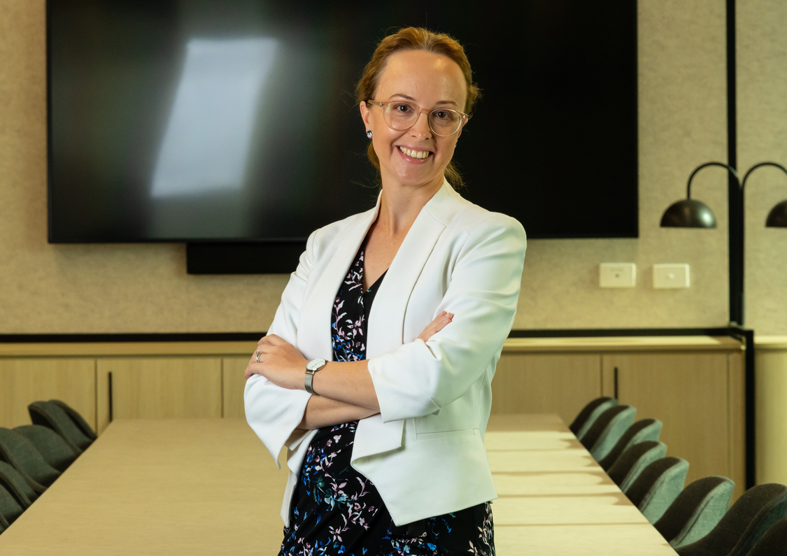 Special Counsel Kylie Dunn wearing a white blazer standing with arms crossed and smiling in the middle of a boardroom