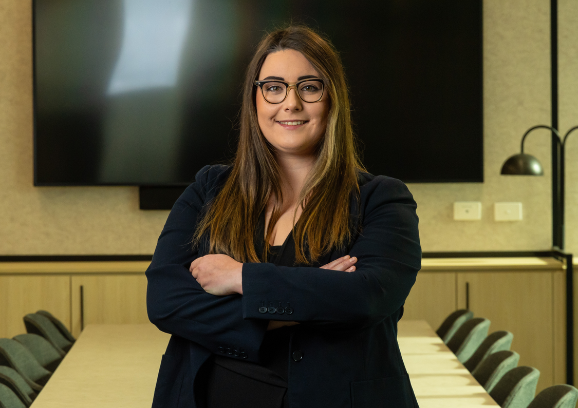 Senior Associate Jessica Punch standing in the middle of a boardroom smiling with her arms folded
