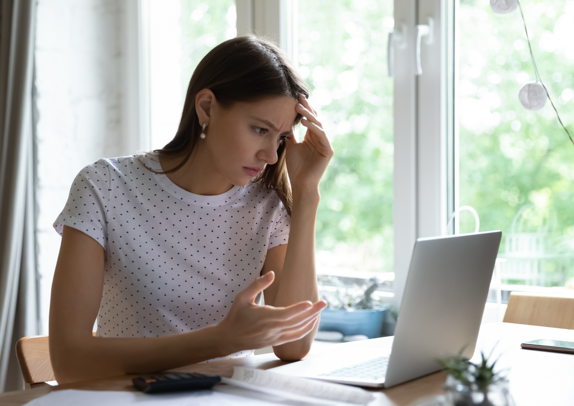 Young woman frowning at her laptop in a home office setting.