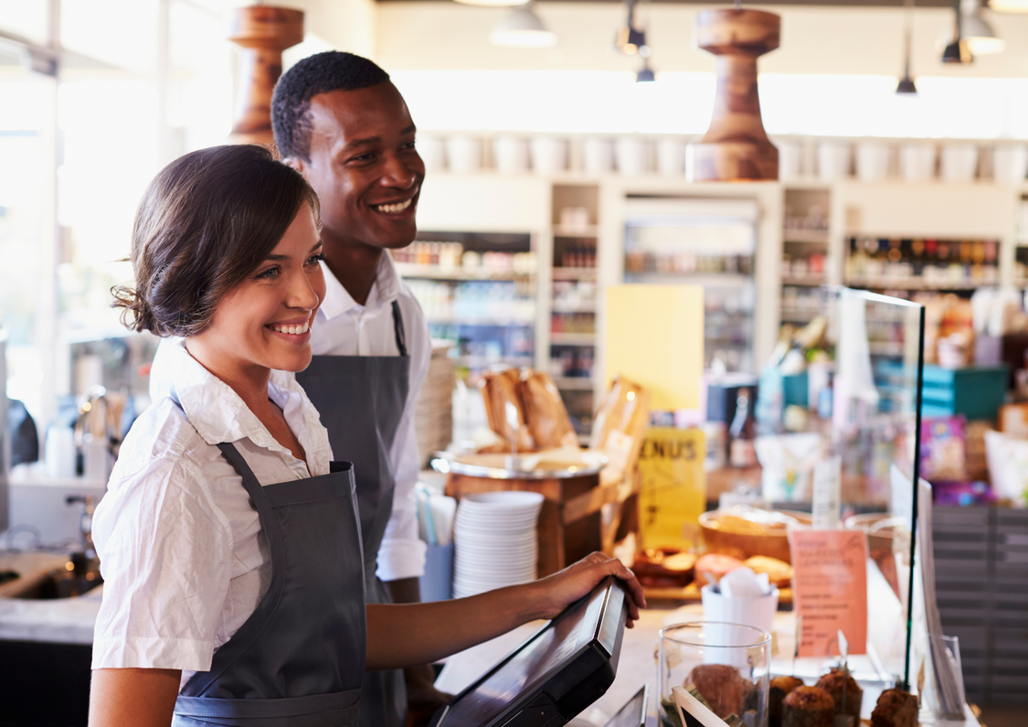 Two young retail workers in aprons smiling at patrons