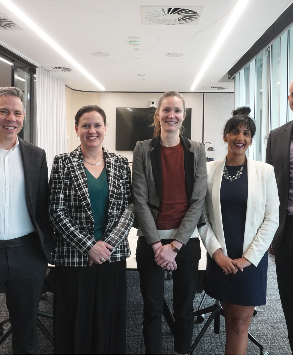 Three women and two men in business attire standing at the end of a boardroom table