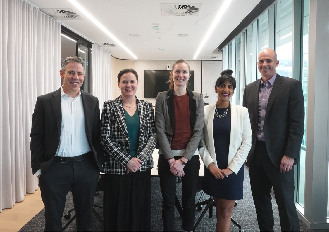 Three women and two men in business attire standing at the end of a boardroom table